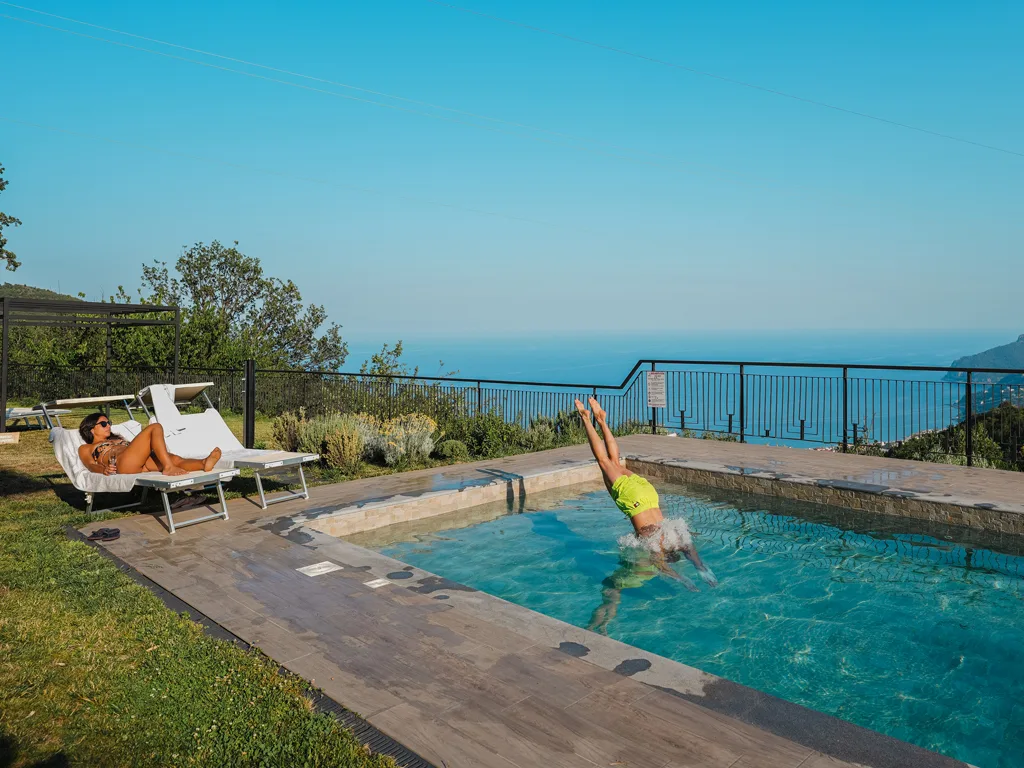 Persone in relax e tuffo in piscina con vista sul mare e la costa
