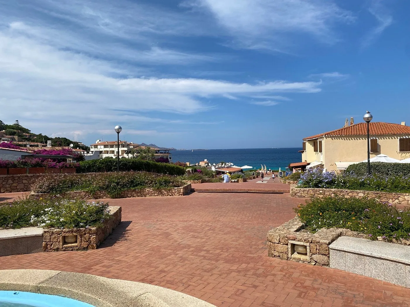 Viale pedonale in mattoni con fiori e vista sul mare blu della Sardegna