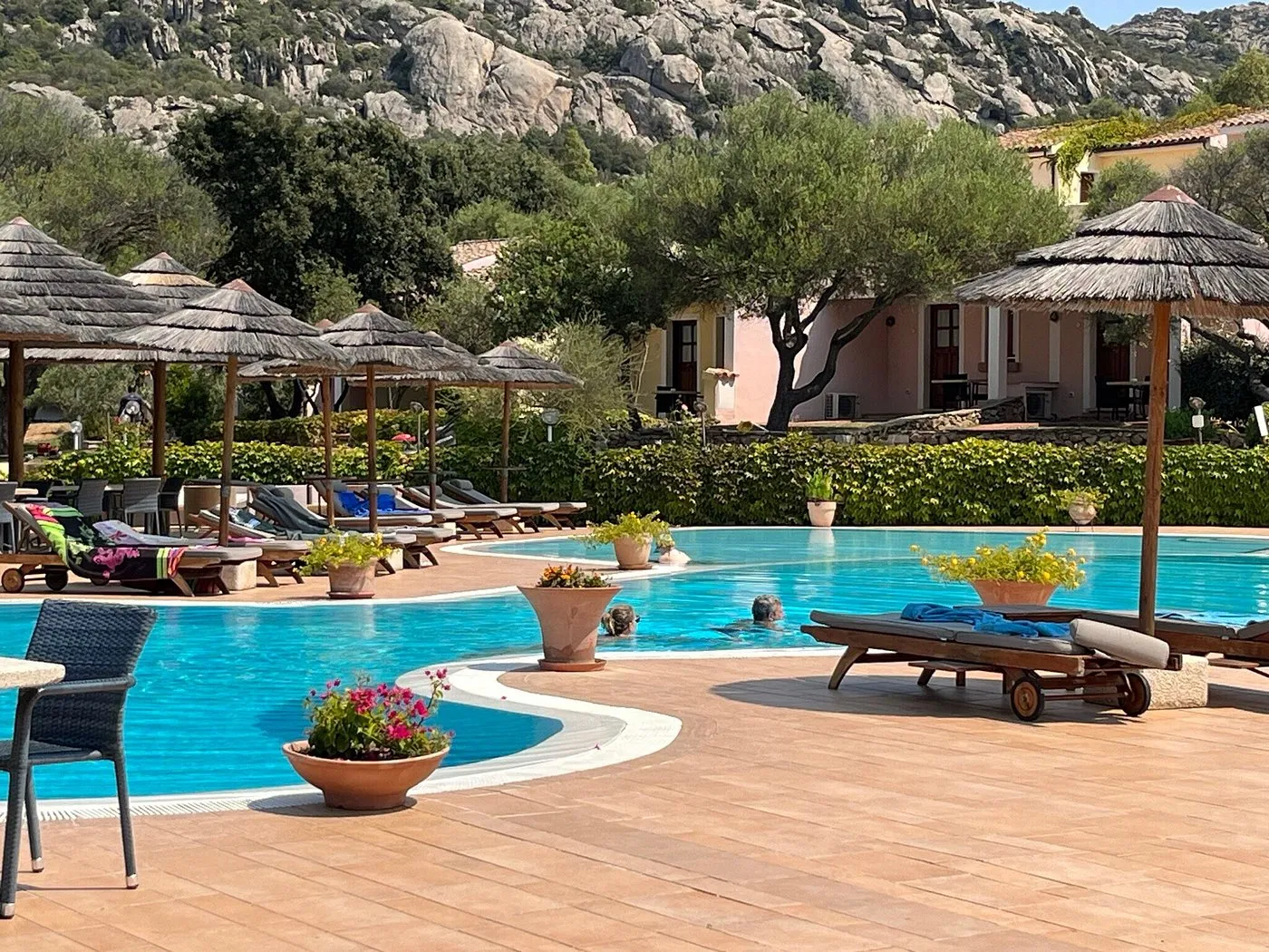 Bordo piscina con lettini e ombrelloni in paglia ai piedi delle montagne rocciose