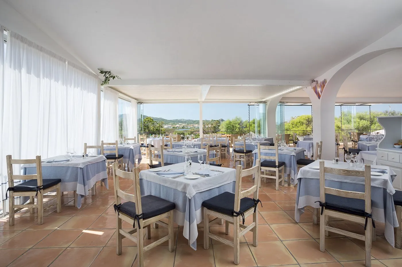 Ristorante con tavoli apparecchiati e tende bianche con vista sul paesaggio