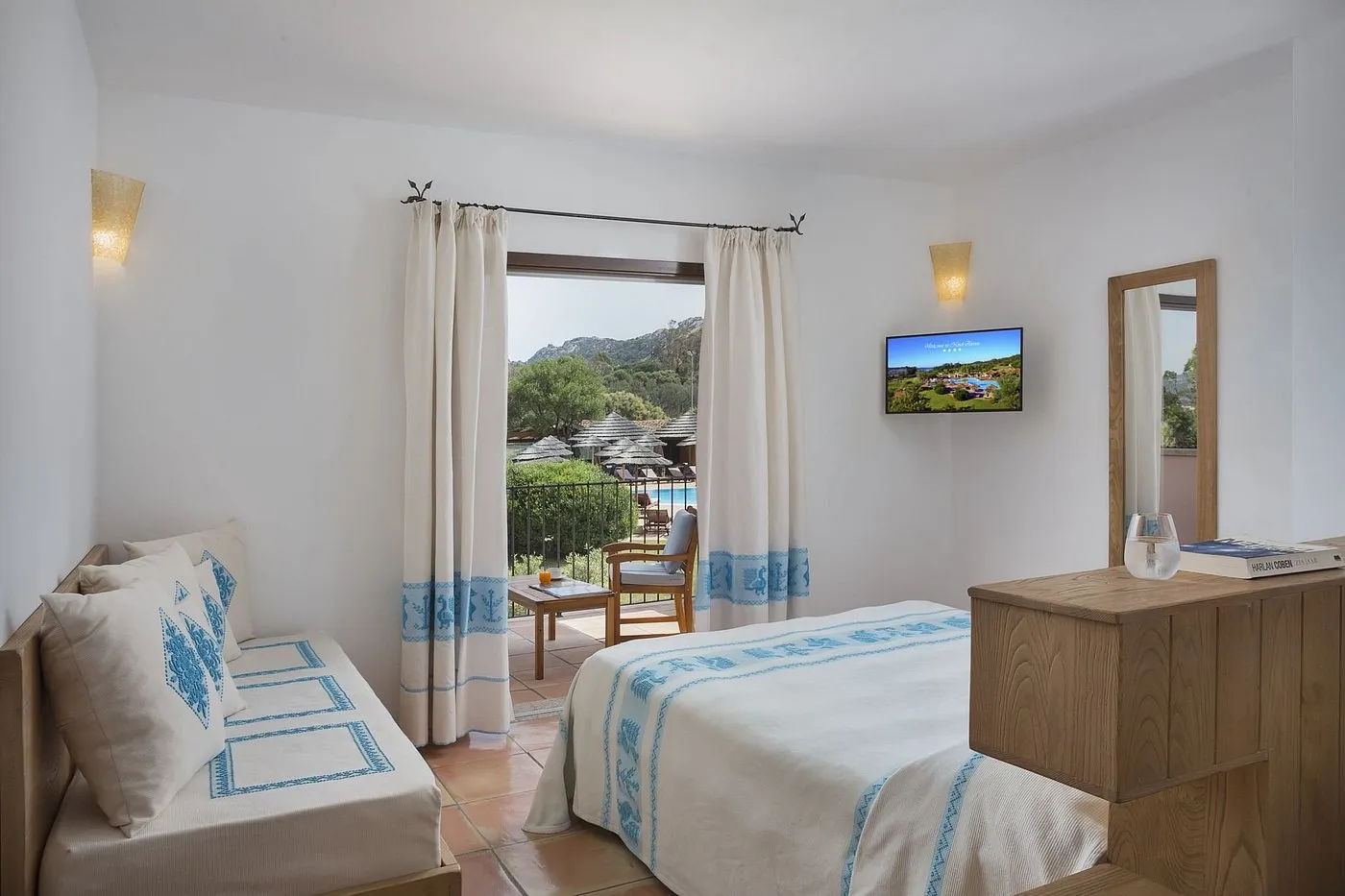 Camera luminosa con letto, divano e balcone con vista sulla piscina e le montagne