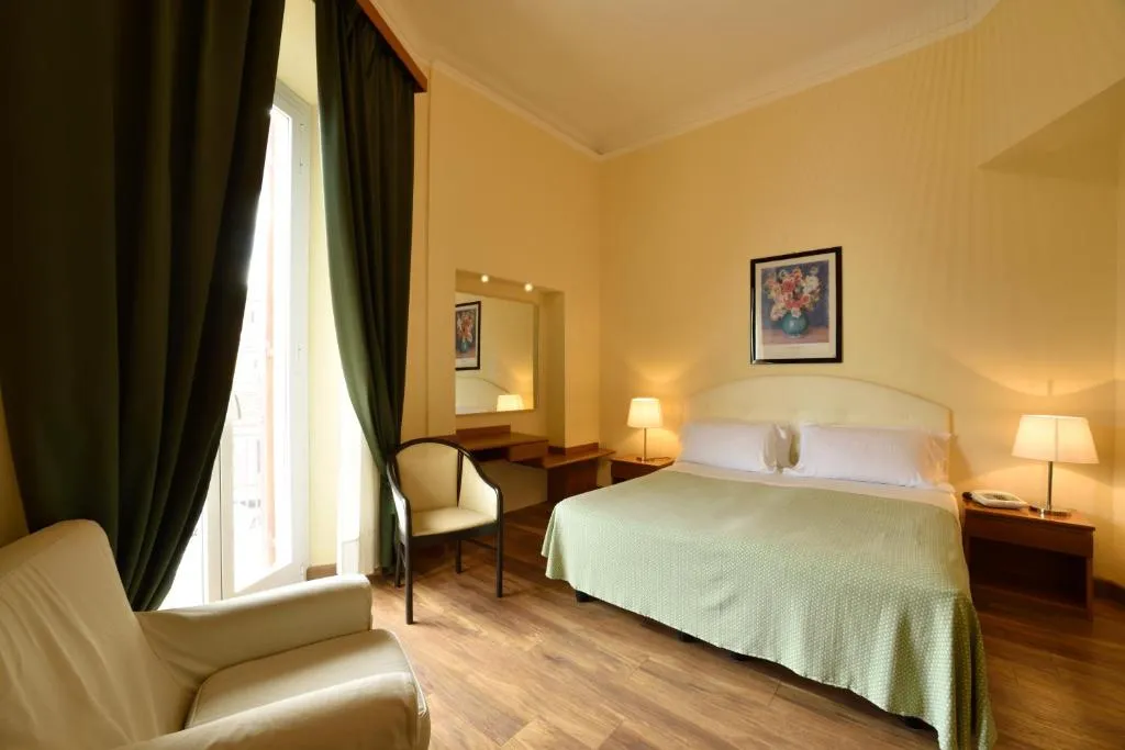 Camera con letto matrimoniale, poltrona, pavimento in parquet e tende verdi