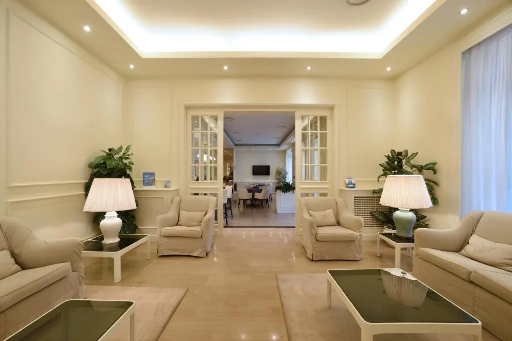 Salotto elegante con poltrone beige, lampade da tavolo, piante e passaggio verso altra sala