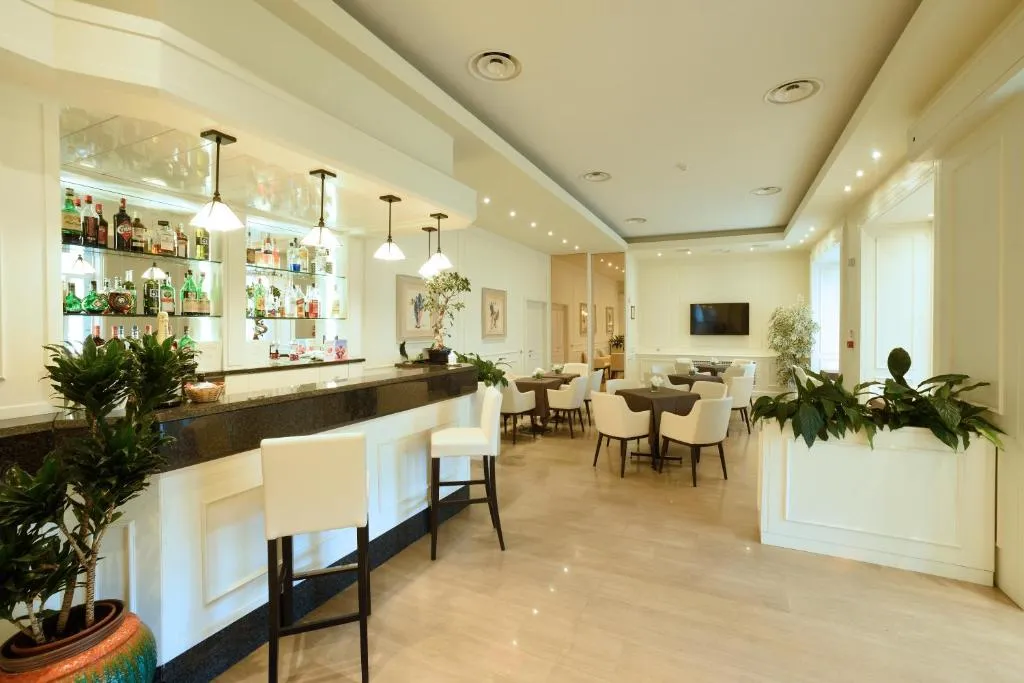 Bar dell'hotel con bancone, sgabelli bianchi, bottiglie esposte e zona tavoli