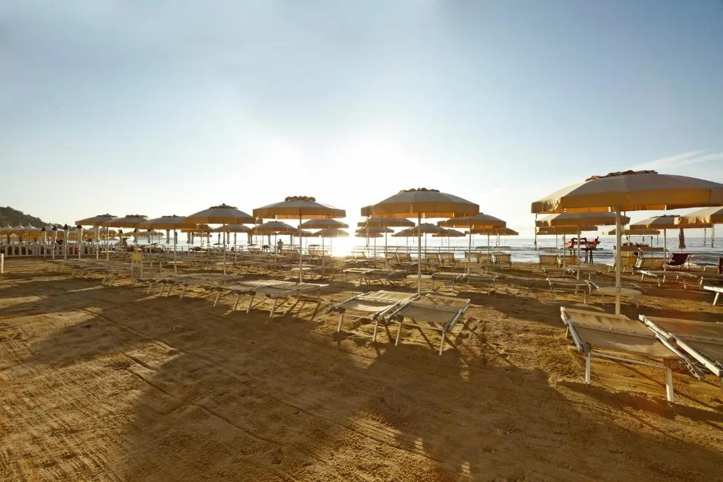 Spiaggia con ombrelloni e lettini controluce con il sole basso sul mare