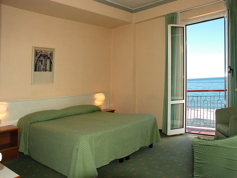 Camera con letto matrimoniale, copriletto verde e balcone con vista sul mare