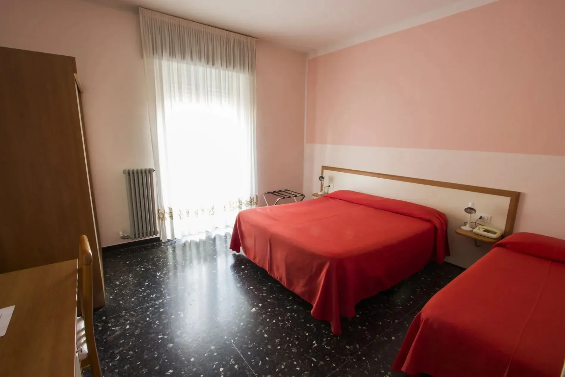 Camera dalle pareti rosa con letto matrimoniale, letto singolo e balcone