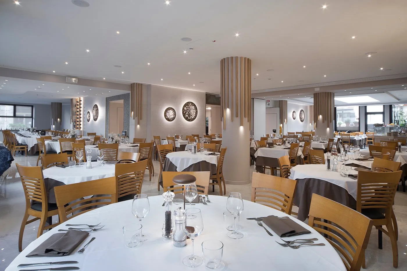 Sala ristorante elegante con tavoli apparecchiati, sedie in legno e illuminazione raffinata
