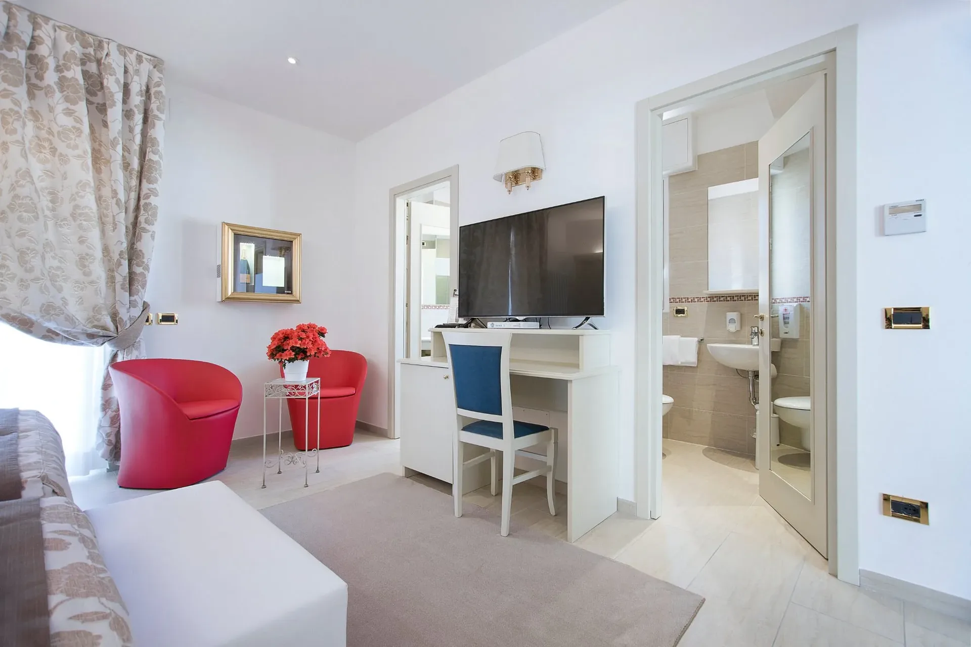 Camera con poltrone rosse, scrivania, TV e bagno privato adiacente