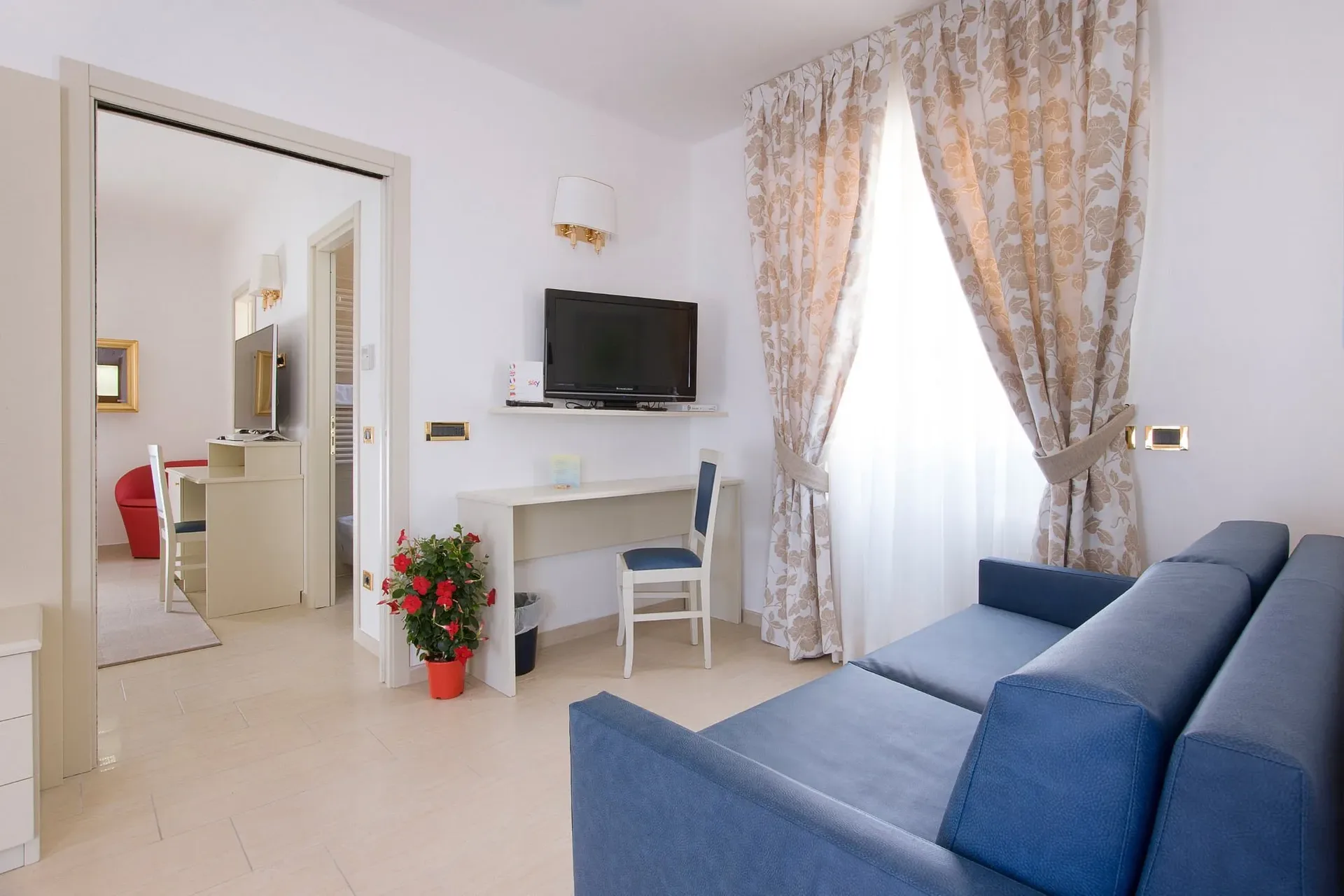 Suite con divano blu, scrivania e camera comunicante con poltrone rosse