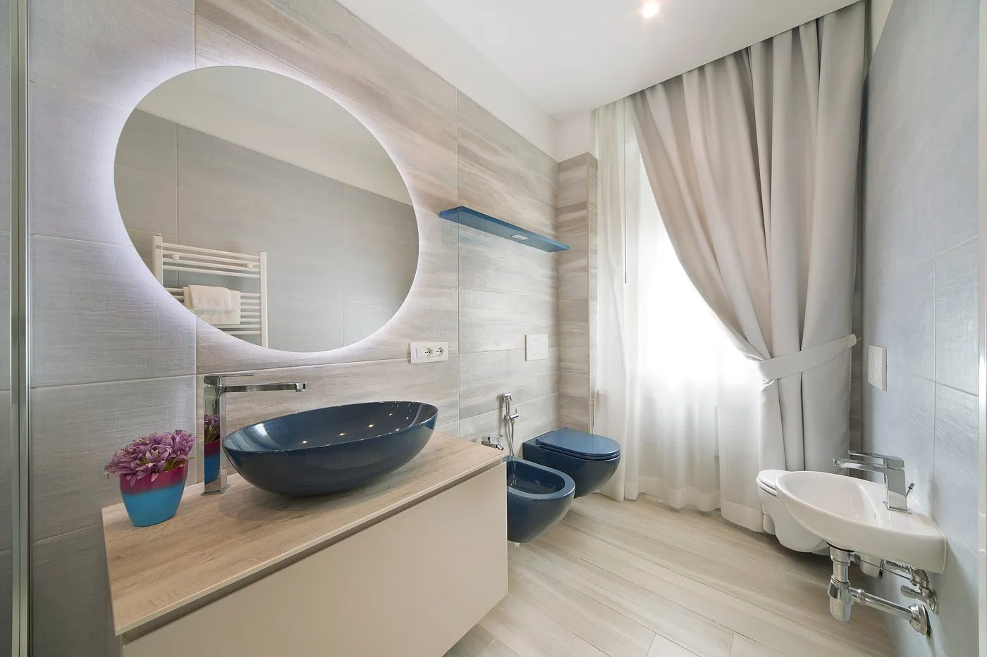 Bagno moderno con lavabo blu, specchio rotondo illuminato e finiture in legno