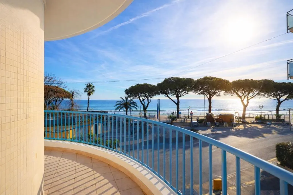Balcone con ringhiera azzurra e vista panoramica sul mare, palme e lungomare