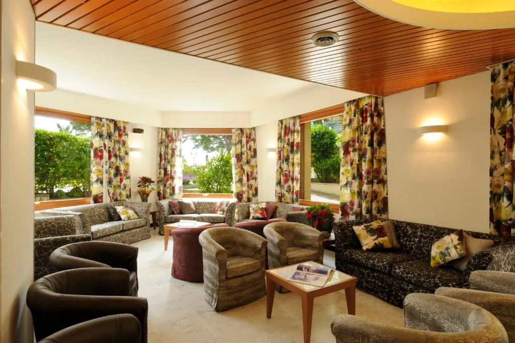 Sala soggiorno con poltrone e divani decorati, tende floreali e finestre affacciate sul giardino