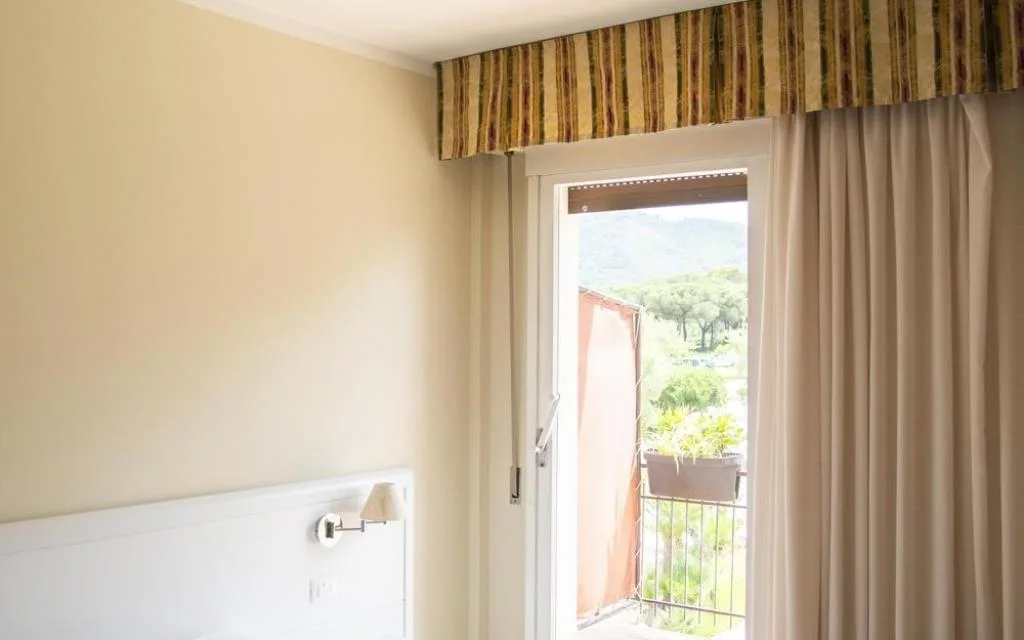 Finestra con tende e balcone affacciato sul giardino e le colline