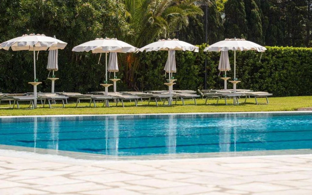 Piscina con lettini e ombrelloni bianchi circondata da vegetazione