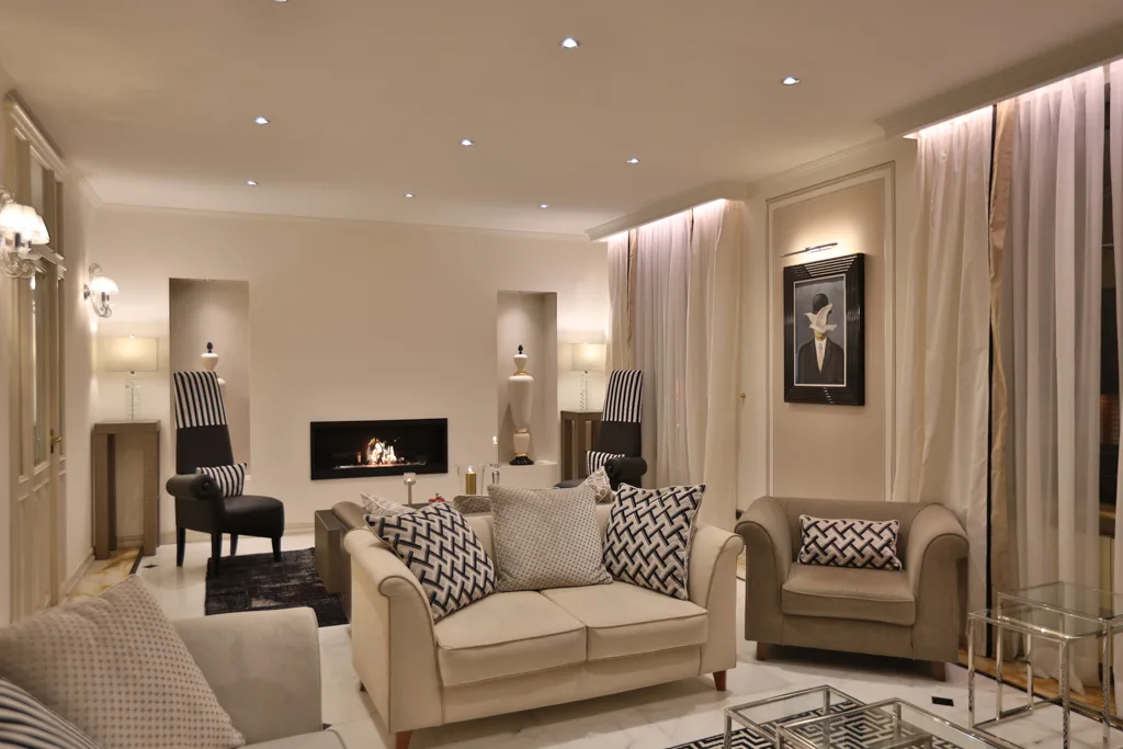 Elegante salotto con divani beige, camino acceso, poltrone a righe e illuminazione soffusa