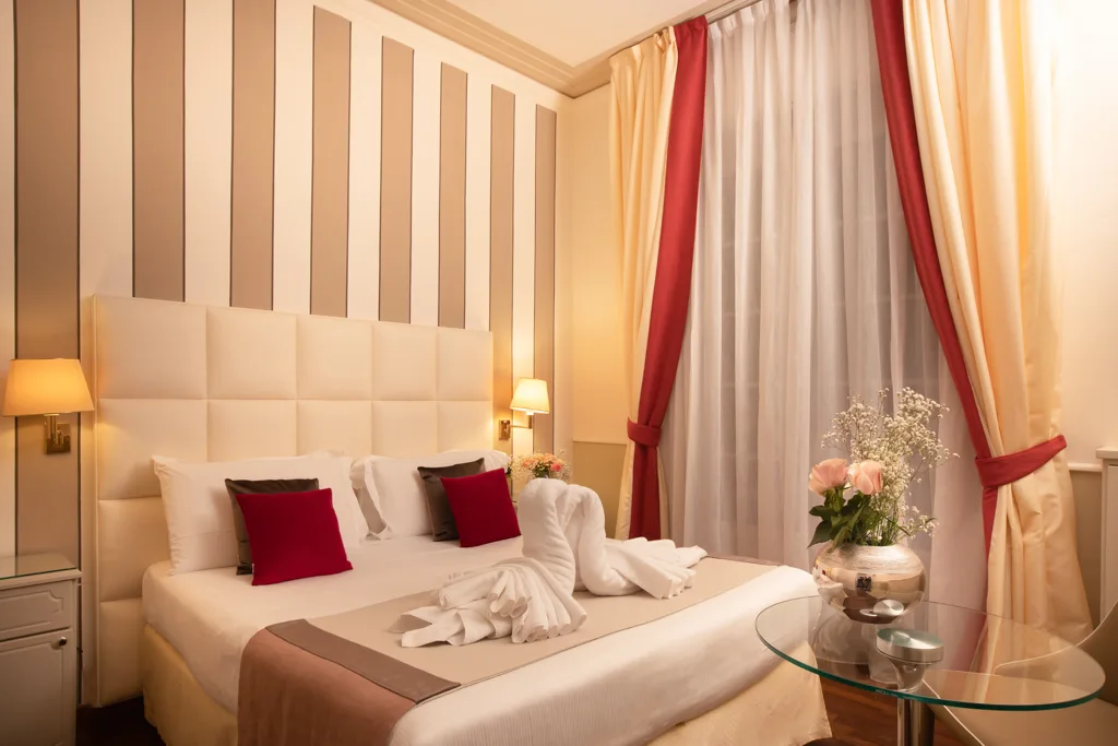 Camera romantica con testiera imbottita, cuscini rossi, tende con drappeggio e fiori freschi