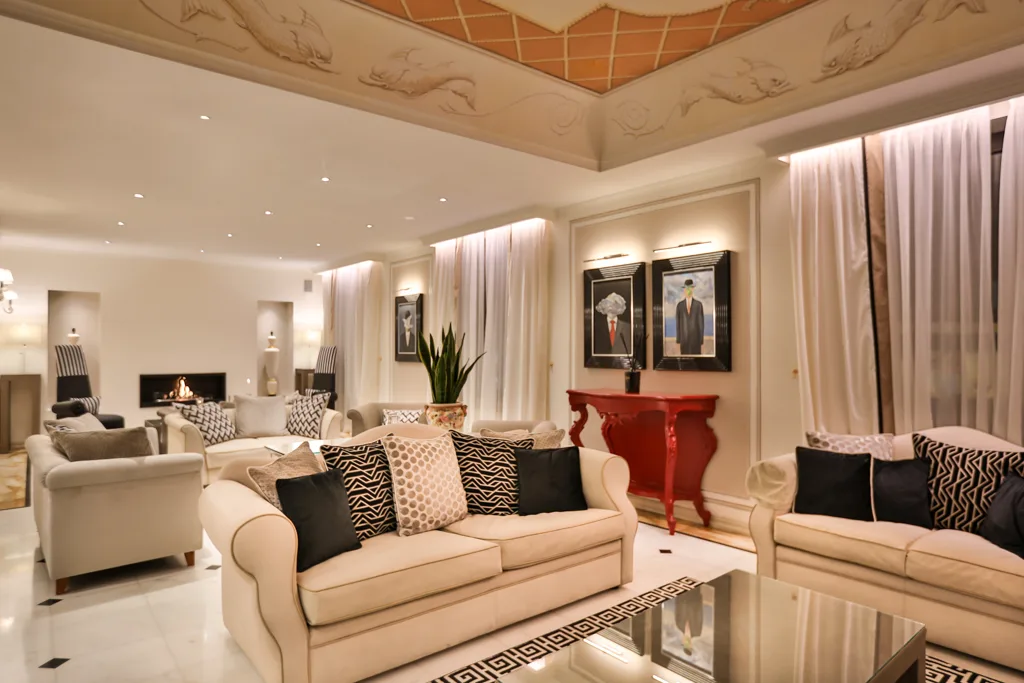 Ampia sala soggiorno elegante con divani beige, camino, soffitto decorato e consolle rossa