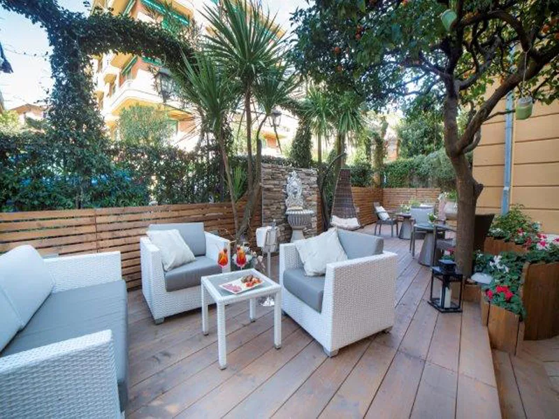 Patio esterno in legno con poltrone bianche in rattan, piante verdi e aperitivo servito