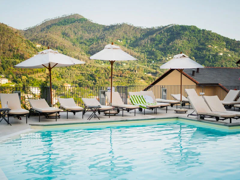 Piscina esterna con lettini, ombrelloni bianchi e panorama sulle montagne verdi