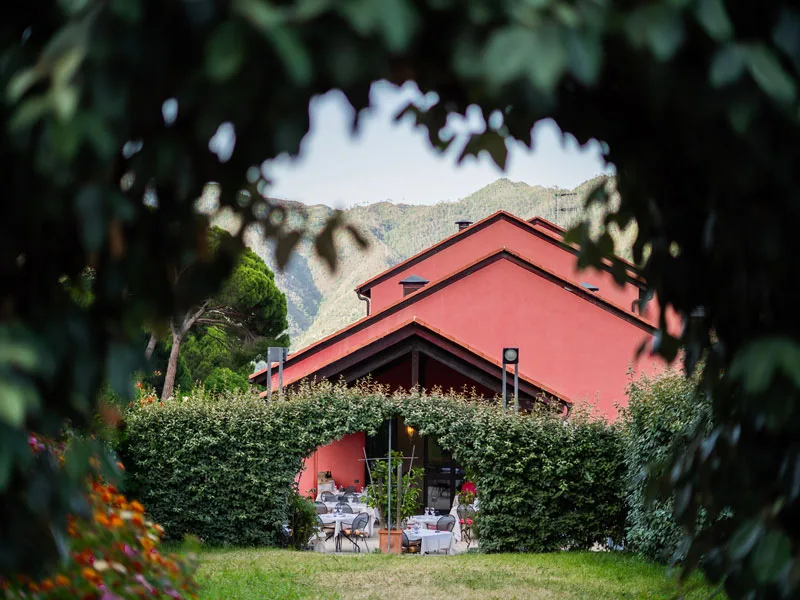Edificio color terracotta del ristorante con terrazza immerso nel verde e sfondo montuoso