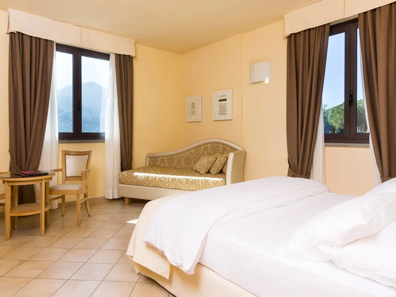 Camera luminosa con letto, divanetto dorato e due finestre con vista sulle montagne