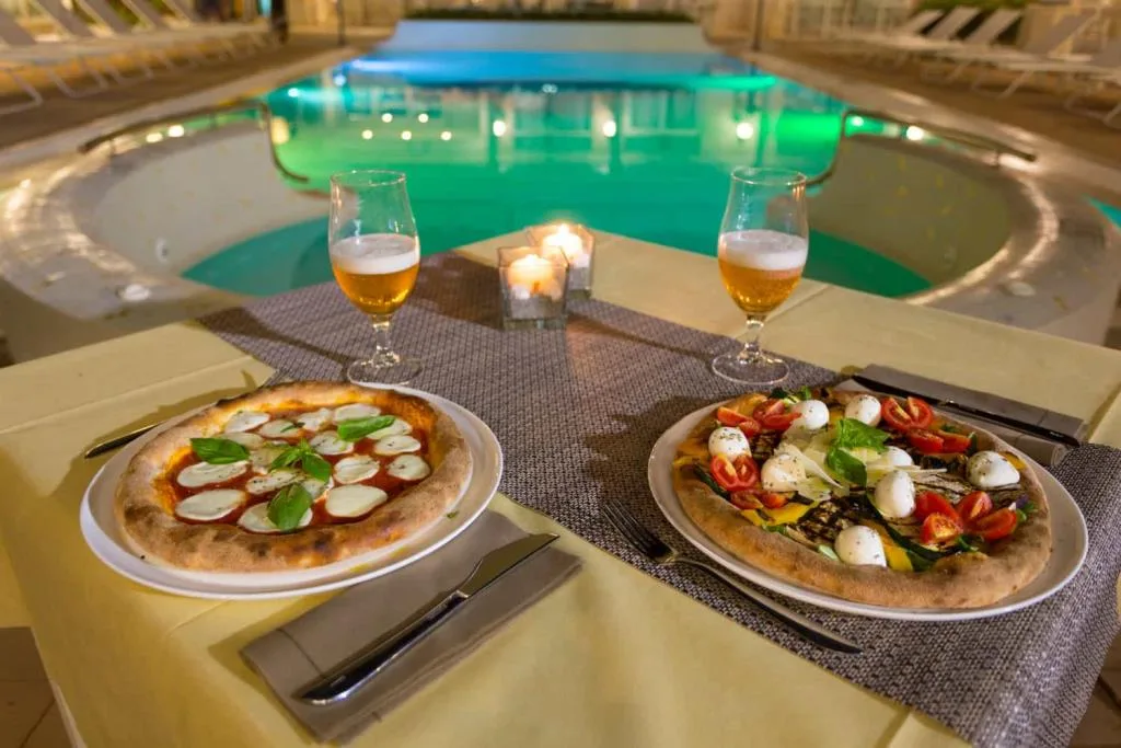 Pizze e birre serviti a bordo piscina illuminata di sera