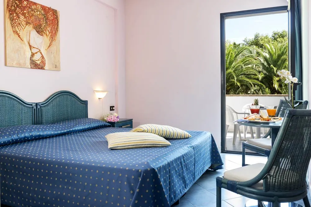 Camera con letto matrimoniale, copriletto blu e balcone affacciato sul verde