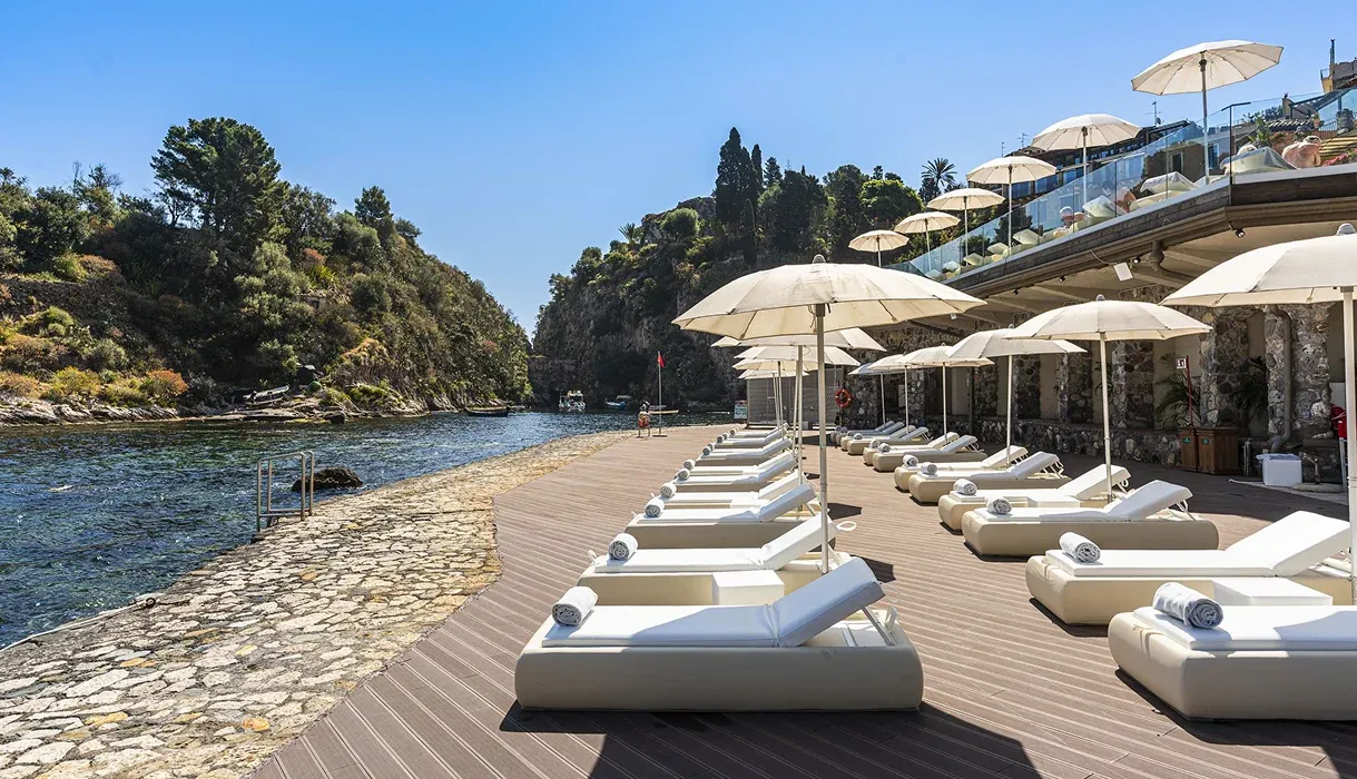 Solarium in legno con lettini bianchi e ombrelloni lungo la caletta di mare
