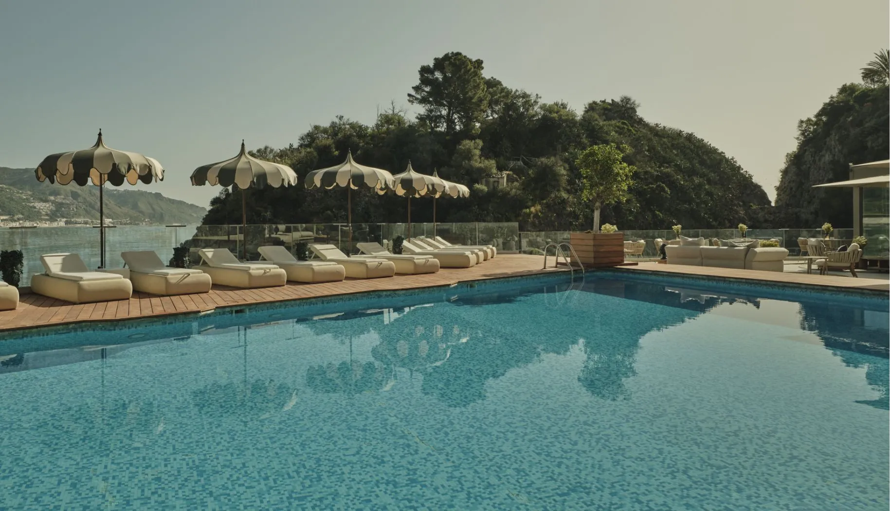 Piscina esterna con lettini bianchi e ombrelloni decorativi affacciata sulla baia