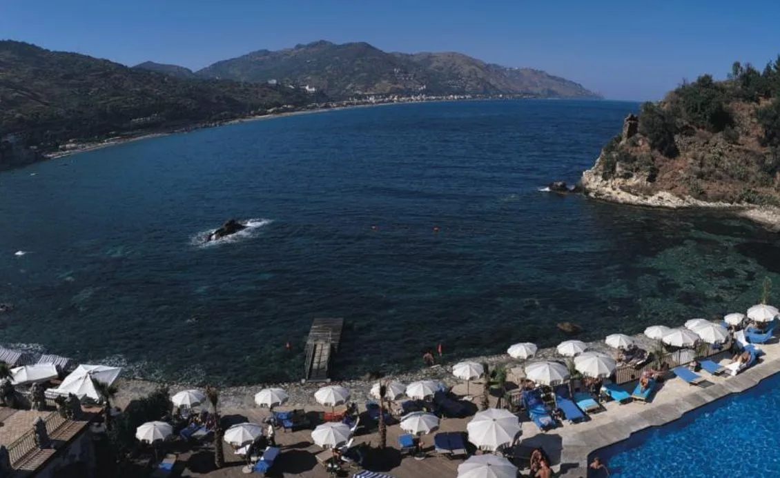 Panorama della baia con piscina, ombrelloni bianchi e lettini affacciati sul mare