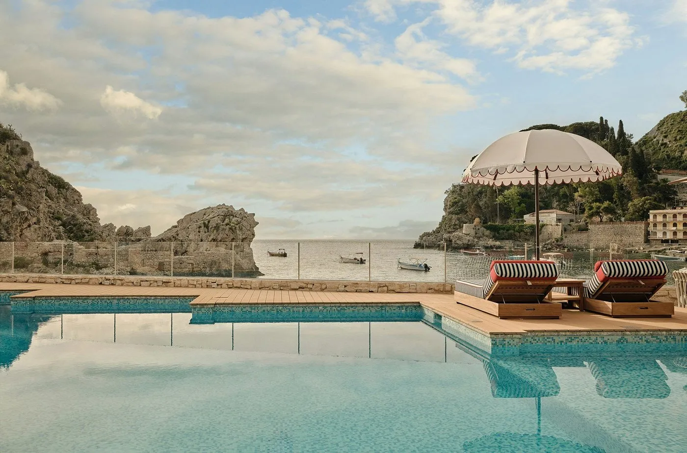 Piscina panoramica con lettini a righe e ombrellone vista baia con barche