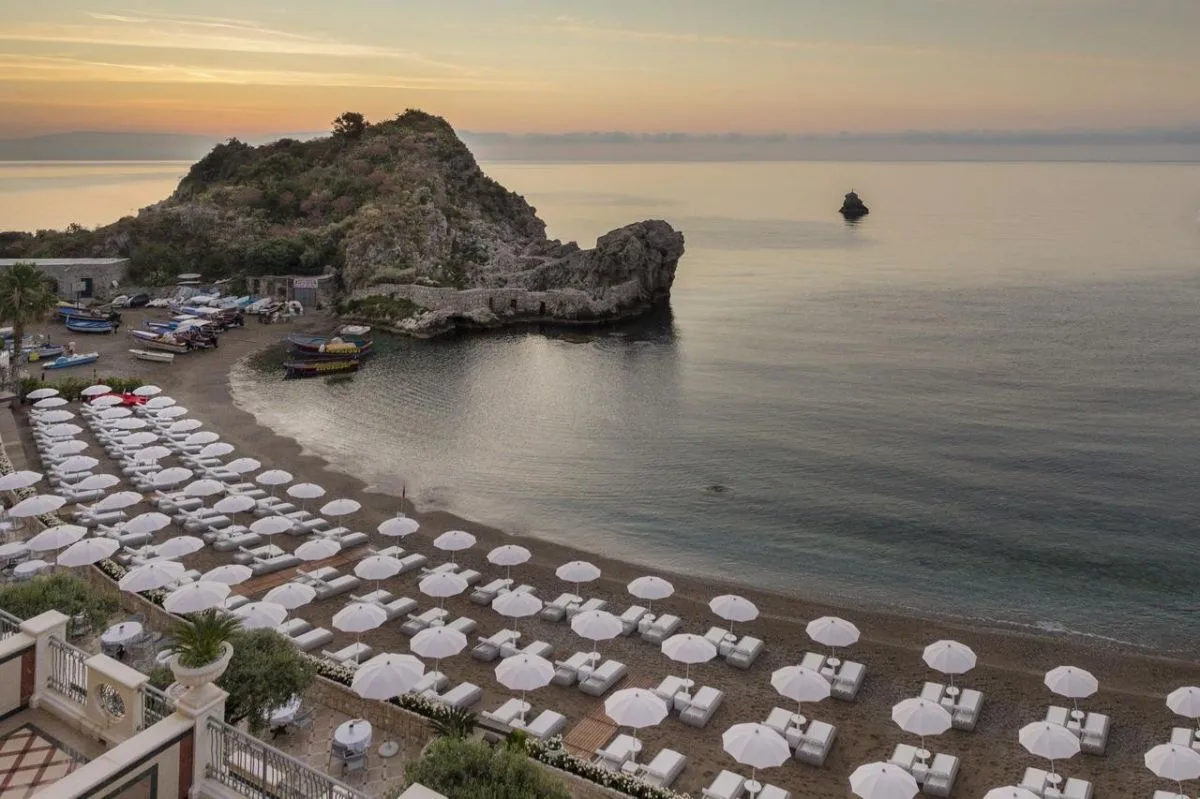 Spiaggia privata con lettini e ombrelloni bianchi affacciata sulla baia al tramonto