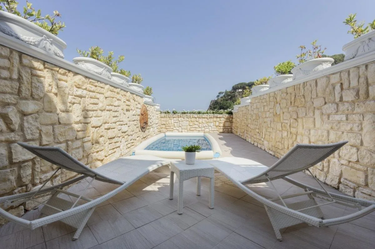 Piccola piscina privata con lettini bianchi circondata da muri in pietra