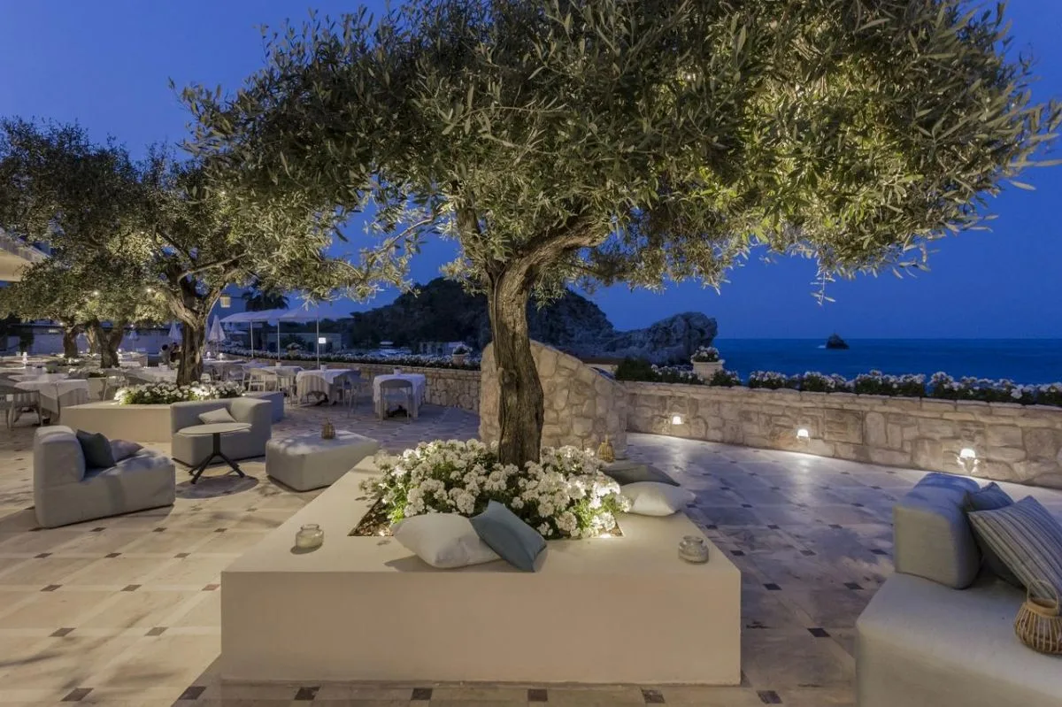 Terrazza lounge serale con ulivi illuminati e divani vista mare
