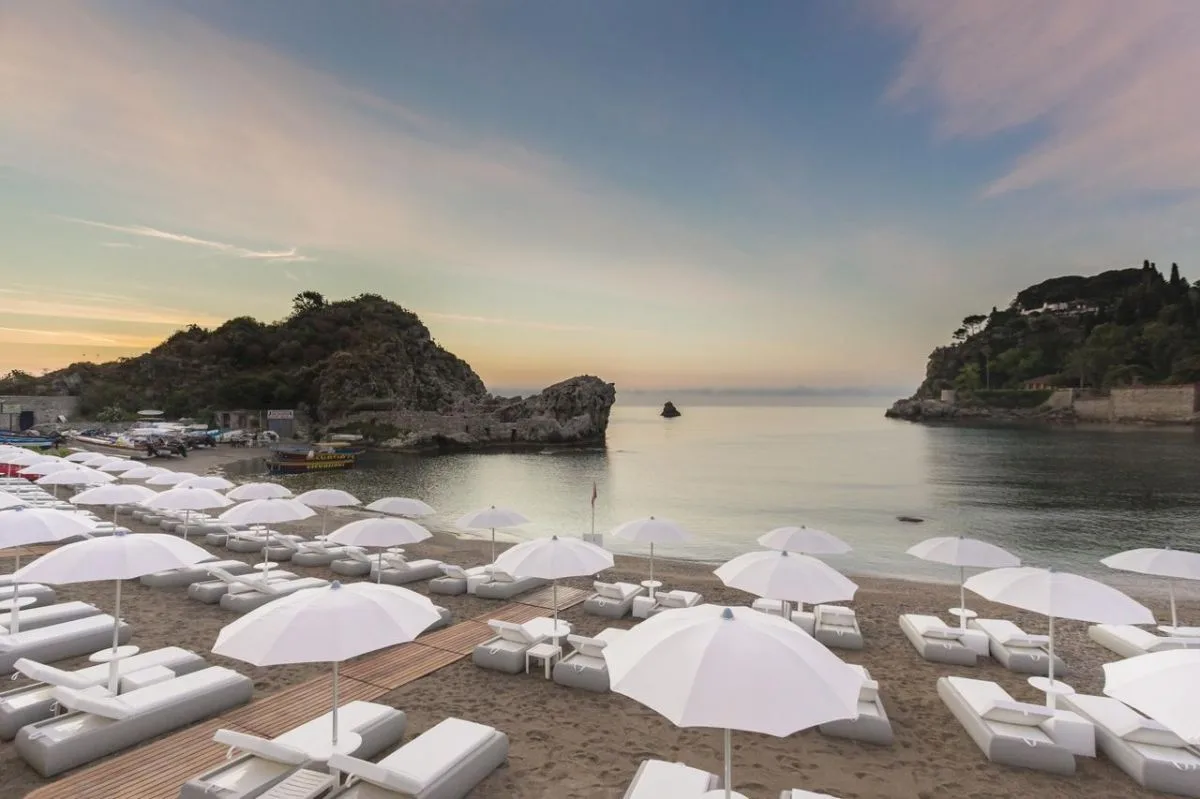 Spiaggia sabbiosa con file di ombrelloni bianchi vista baia al crepuscolo