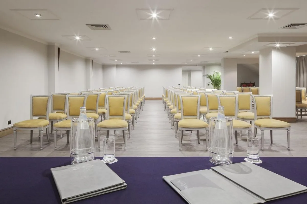 Sala meeting allestita a platea con sedie gialle e tavolo relatore