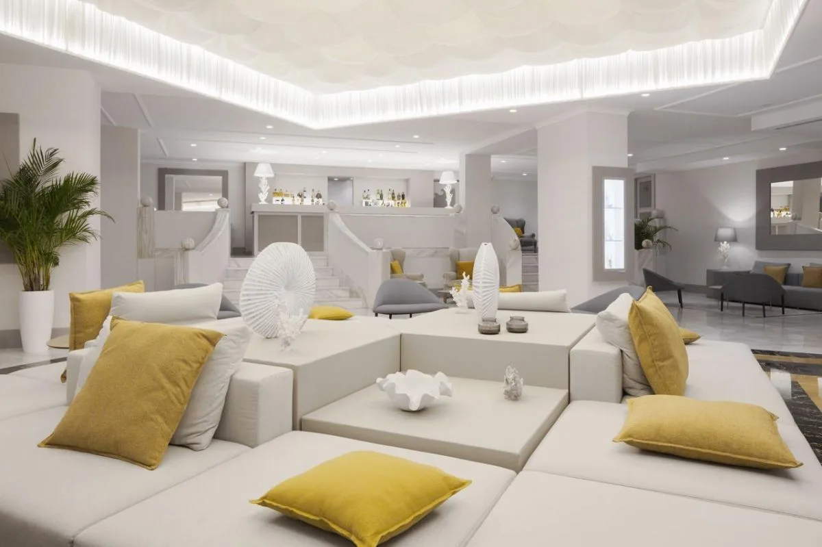 Lobby lounge moderna con divani bianchi, cuscini gialli e illuminazione soffusa