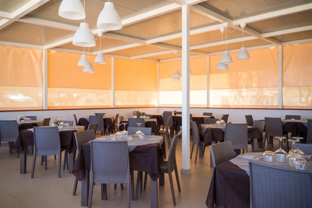 Sala ristorante con tavoli apparecchiati, sedie in rattan e ampie vetrate luminose
