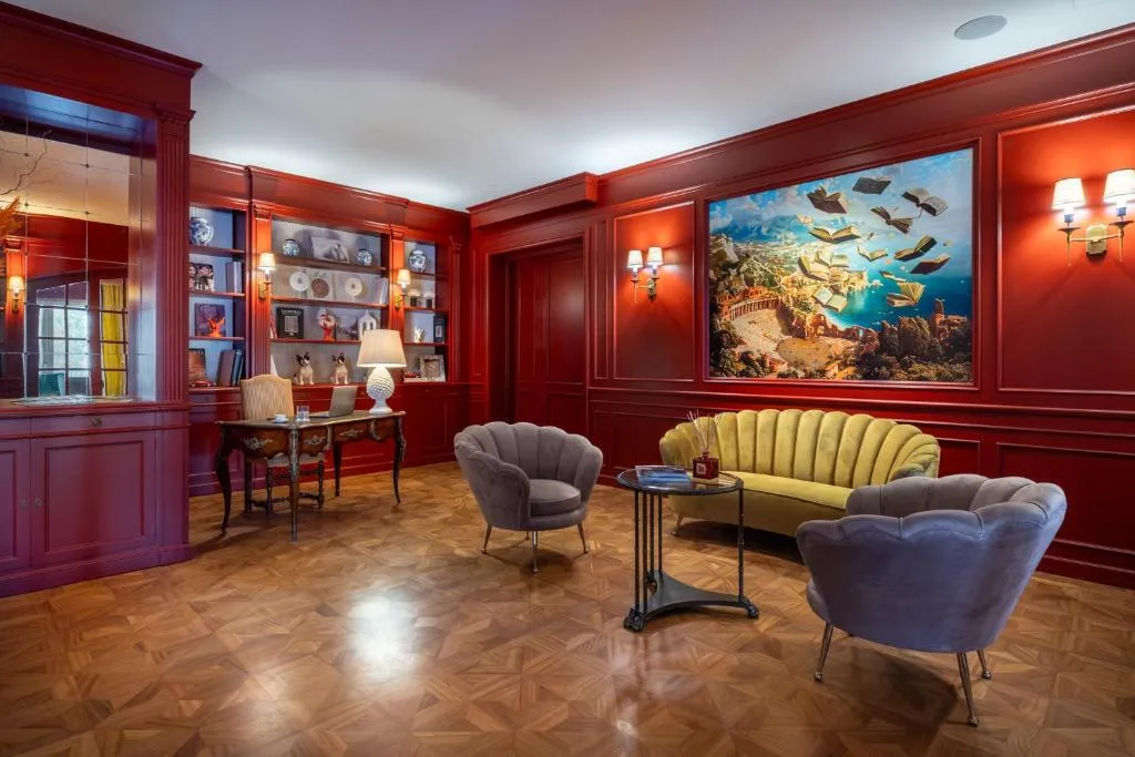 Sala lettura con pareti rosse, poltrone velluto e grande quadro decorativo