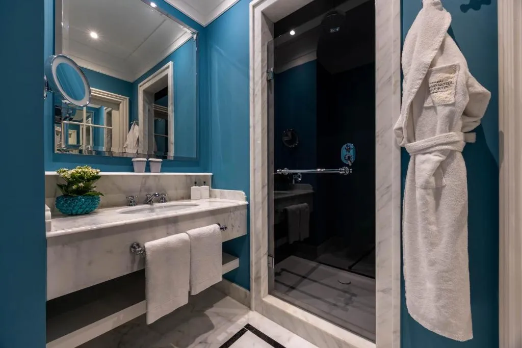 Bagno con pareti blu, lavabo in marmo, doccia e accappatoio