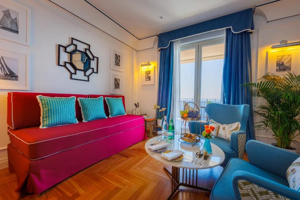 Soggiorno della suite con divano rosso, poltrone blu e balcone