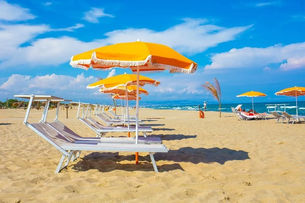 Spiaggia di sabbia con lettini e ombrelloni gialli sotto il cielo azzurro