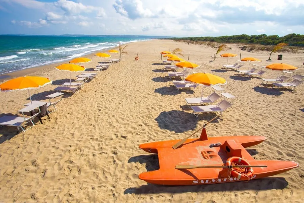 Ampia spiaggia con file di ombrelloni arancioni e pattino di salvataggio