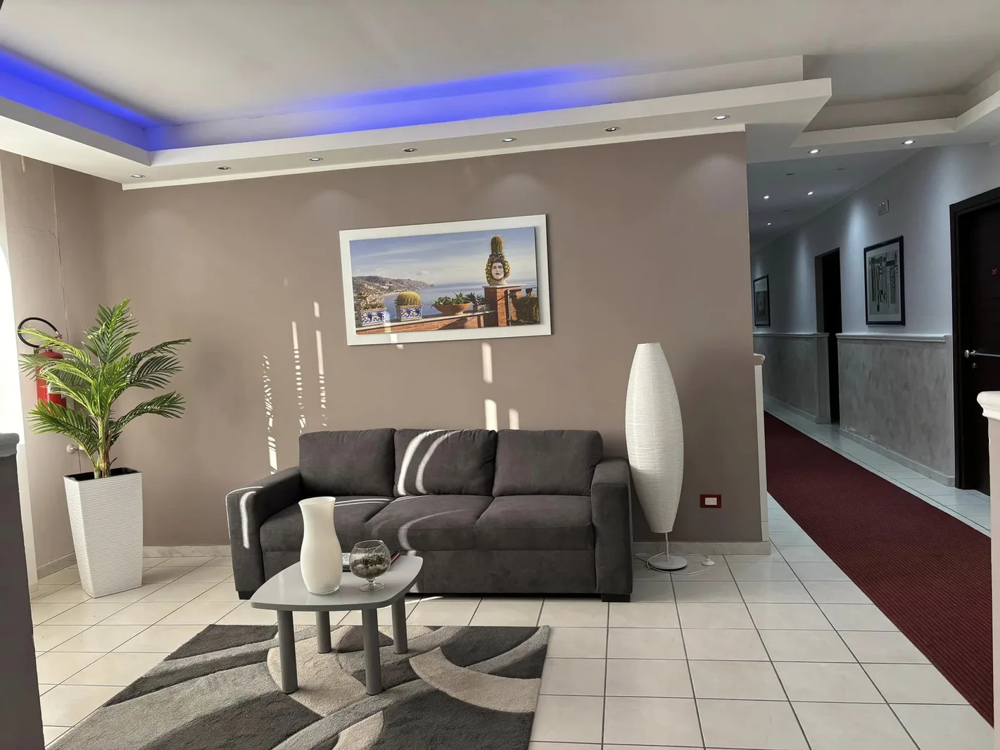 Area lounge con divano grigio, tavolino e corridoio con tappeto rosso