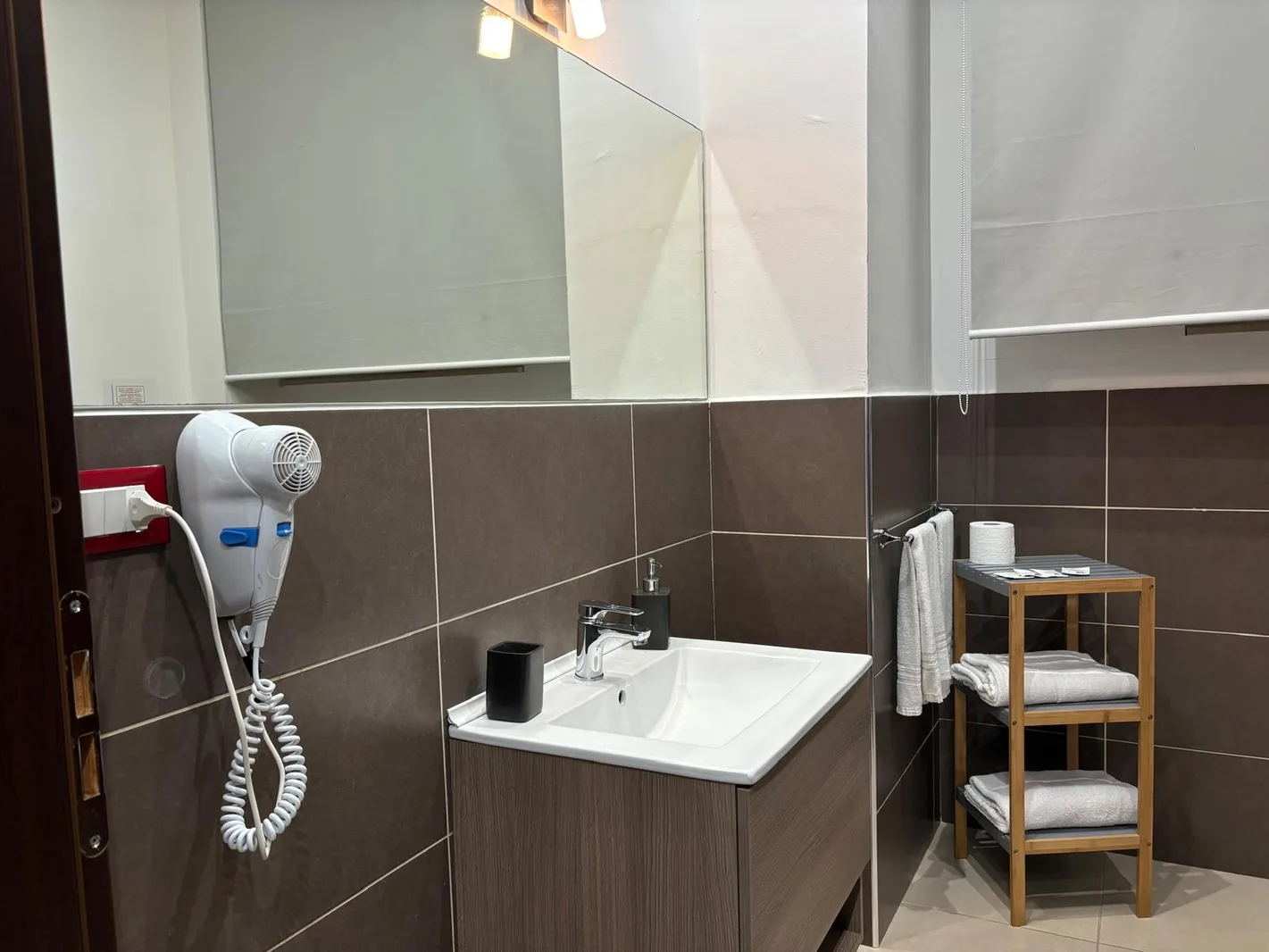 Bagno con lavabo, specchio, asciugacapelli e mensole con asciugamani