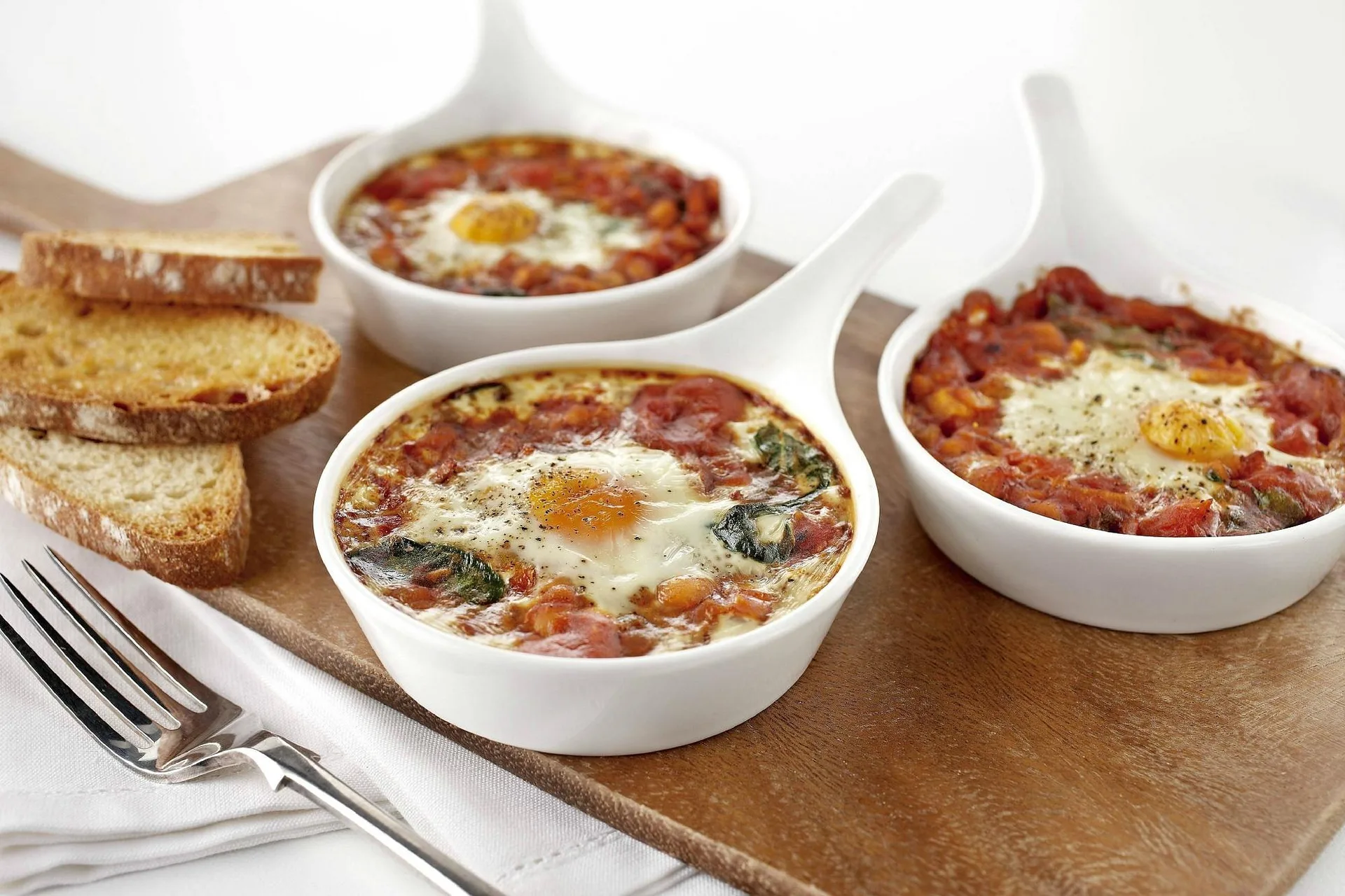 Uova al pomodoro con spinaci in tegamini e fette di pane tostato